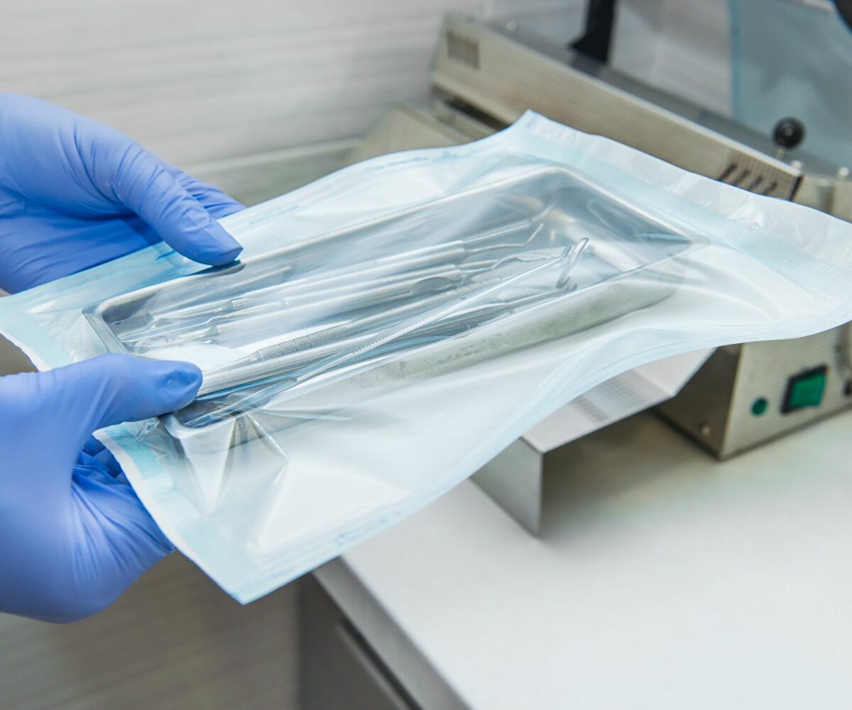 Close up dentist assistant's hands holding packaged with vacuum packing machine medical instruments ready for sterilizing in autoclave. Dental office. Selective focus, space for text